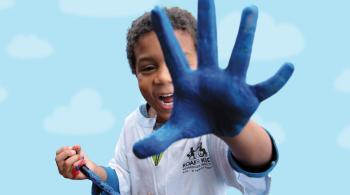一个孩子右手拿着画笔，左手对着相机，手掌上涂满了蓝色的颜料